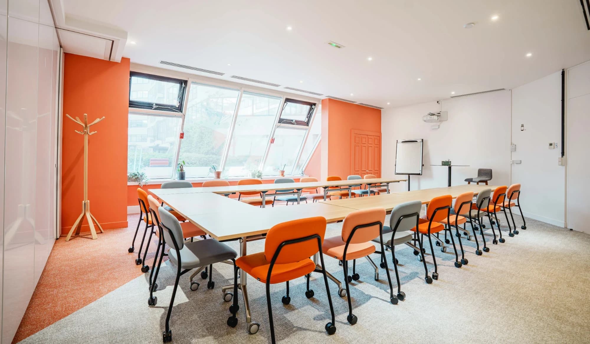Salle de réunion du Wojo Issy-les-Moulineaux : tables en U, chaises orange et grises, murs orange et grandes fenêtres inclinées.