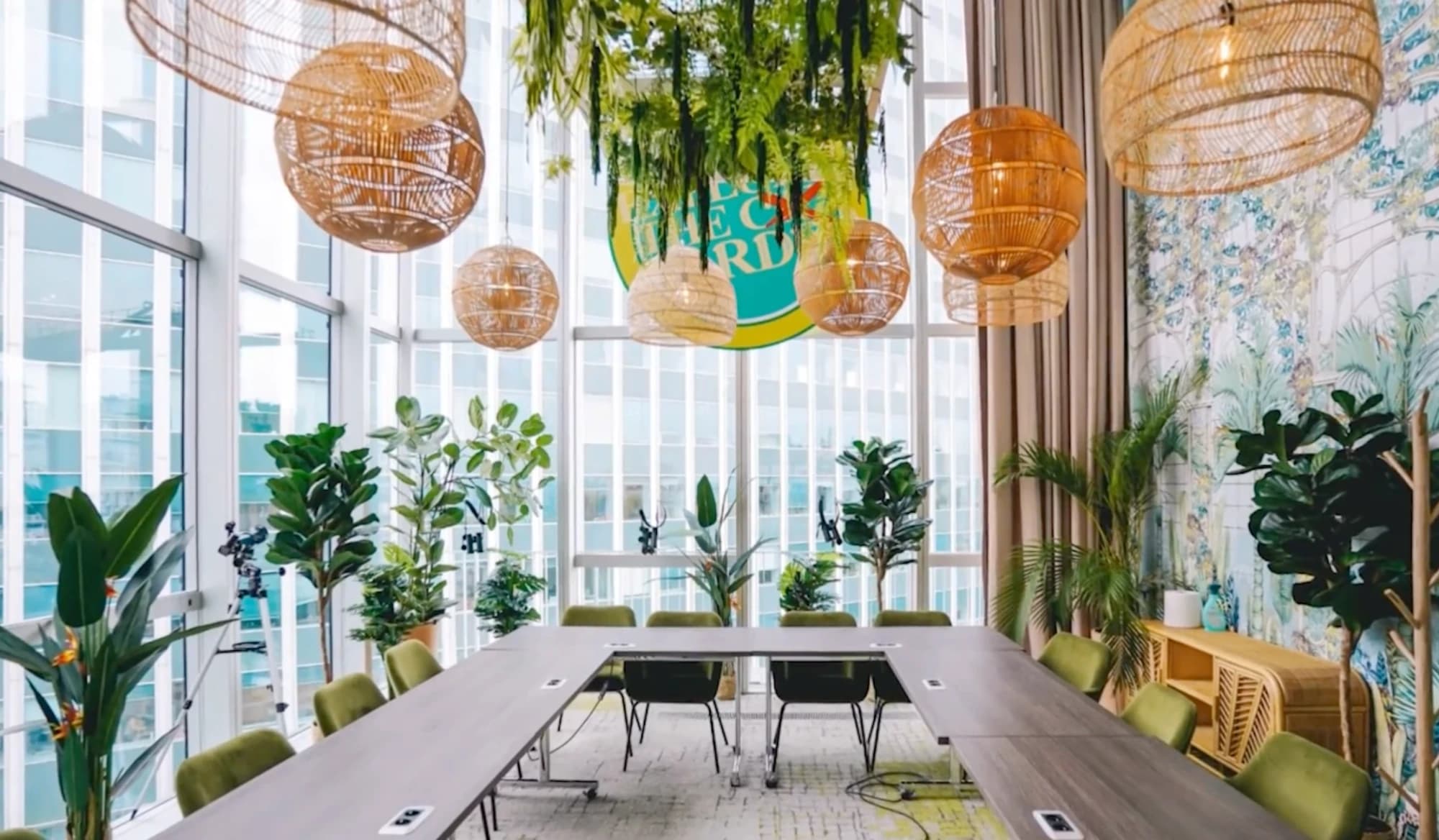 Salle de réunion du Wojo Montparnasse : table en U, chaises vertes, lampes en rotin et baies vitrées.