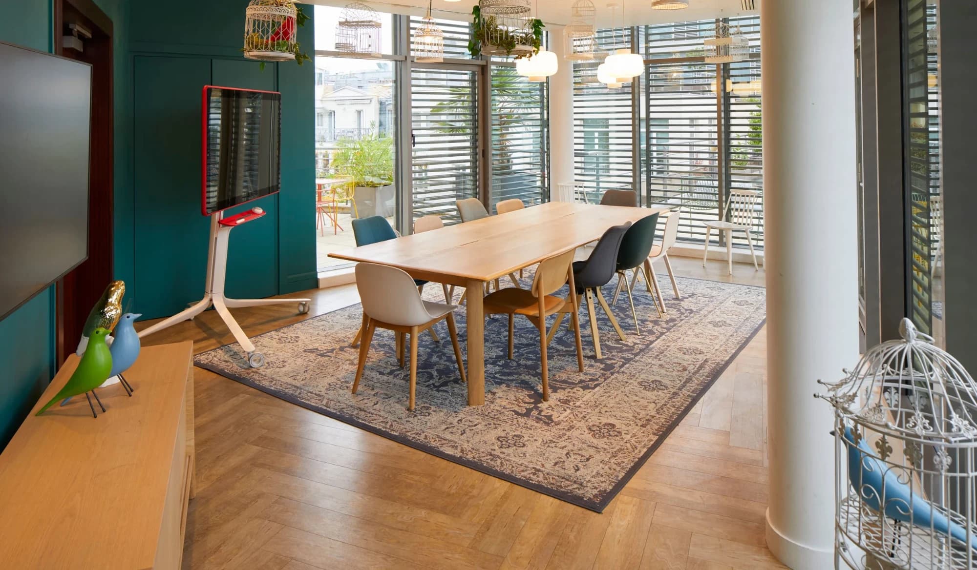Salle de réunion du Wojo Saint-Lazare : grande table en bois, chaises colorées, cages décoratives et baies vitrées sur une terrasse.